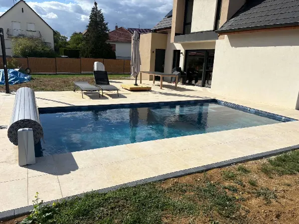 Piscine avec plage en dallage beige au pied d’une maison