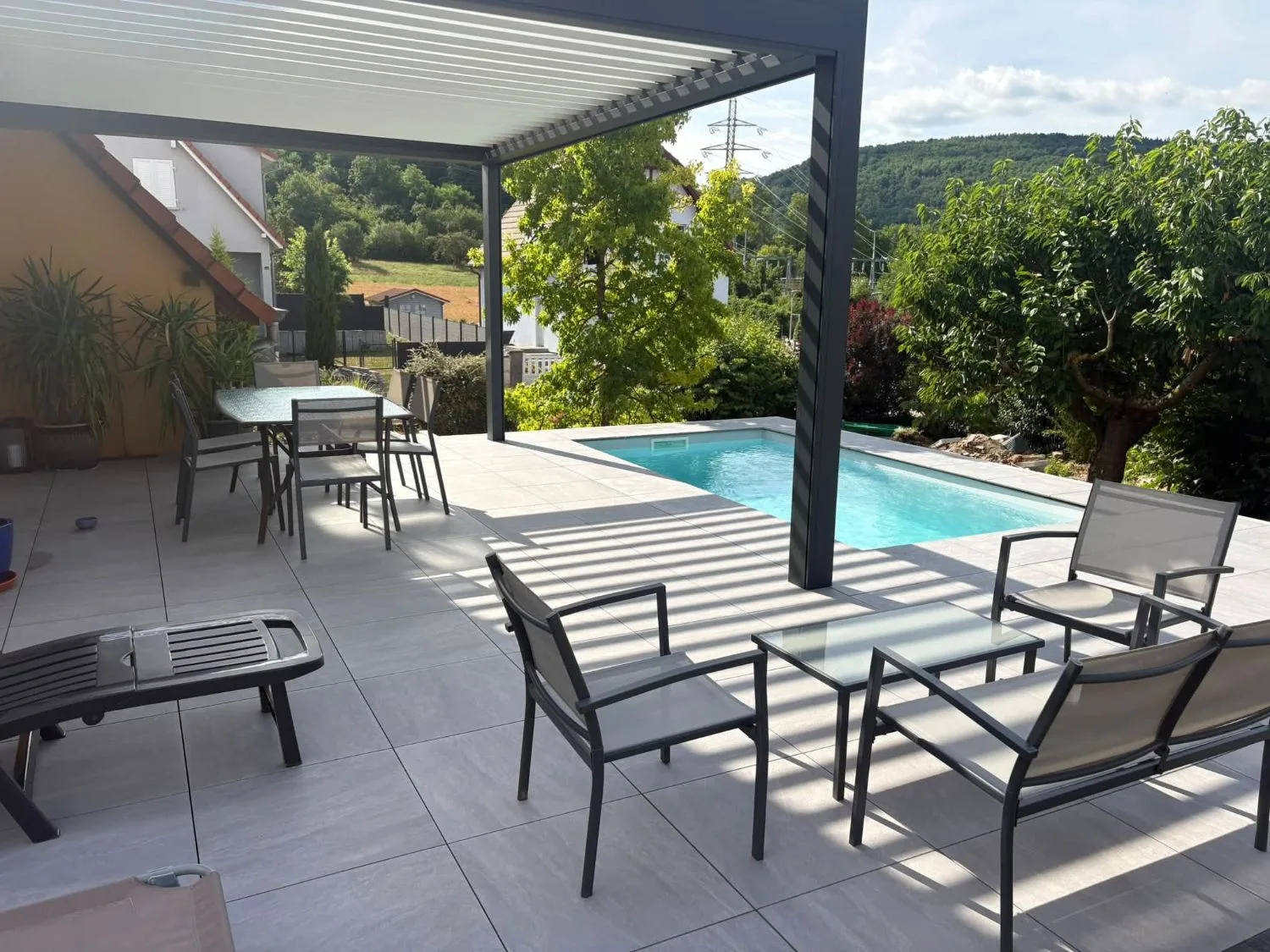 Piscine et terrasse en dallage gris sous une pergola bioclimatique